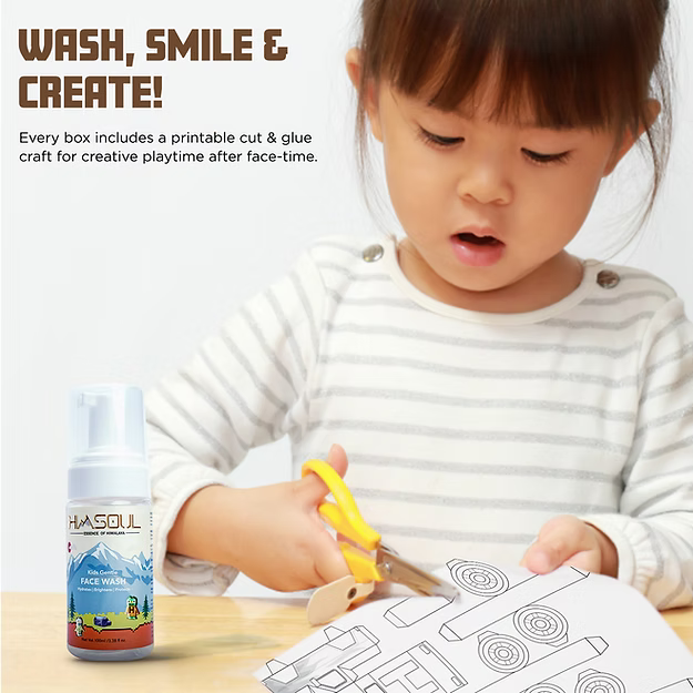 A marketing graphic titled "WASH, SMILE & CREATE!" featuring a young girl in a striped shirt carefully using safety scissors to cut out a paper toy. To the left is a bottle of Himsoul Kids Gentle Face Wash. The text explains that the product's monocarton is designed with a printable cut-and-glue craft, allowing children to repurpose the packaging into toys for creative playtime after their skincare routine.