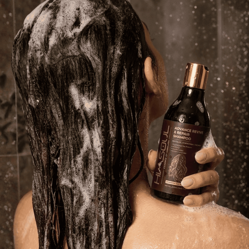 Woman holding Himsoul Advance Revive & Repair Shampoo during a shower, applying rich lather to reinforce weak hair fibers and reduce breakage.
