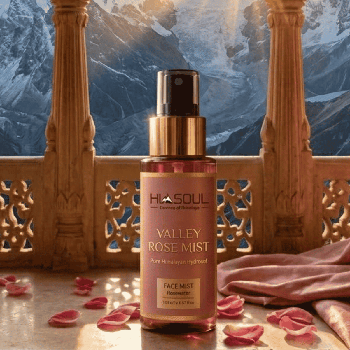 Himsoul Valley Rose Mist amber spray bottle resting on fresh rose petals on a stone pedestal with snowy Himalayan mountains in the background.